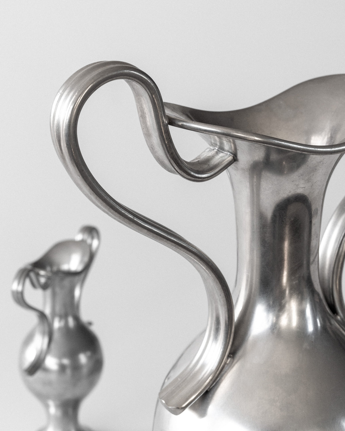 Close-up of Spigel's Pair of Neoclassical Metal Vases, 1953 Sweden, featuring elegant curves and polished surfaces. The larger vase is in focus with the smaller one subtly blurred in the background against a plain white backdrop.