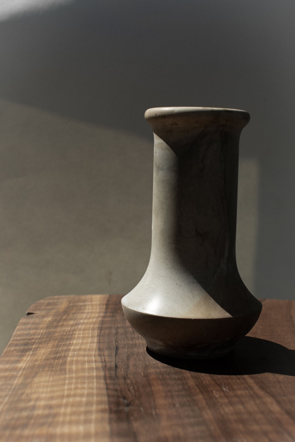 Curved profile of vintage stone vase with flared neck on wood