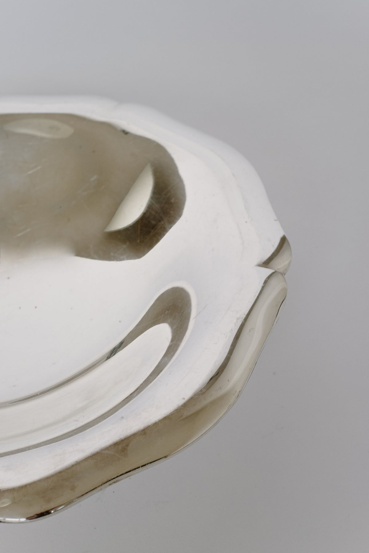 A close-up of a reflective Silverplated Bowl by septembre studios against a plain background showcases its vintage appeal with a scalloped edge and smooth, glossy surface that casts gentle reflections, adding unique character to any setting.