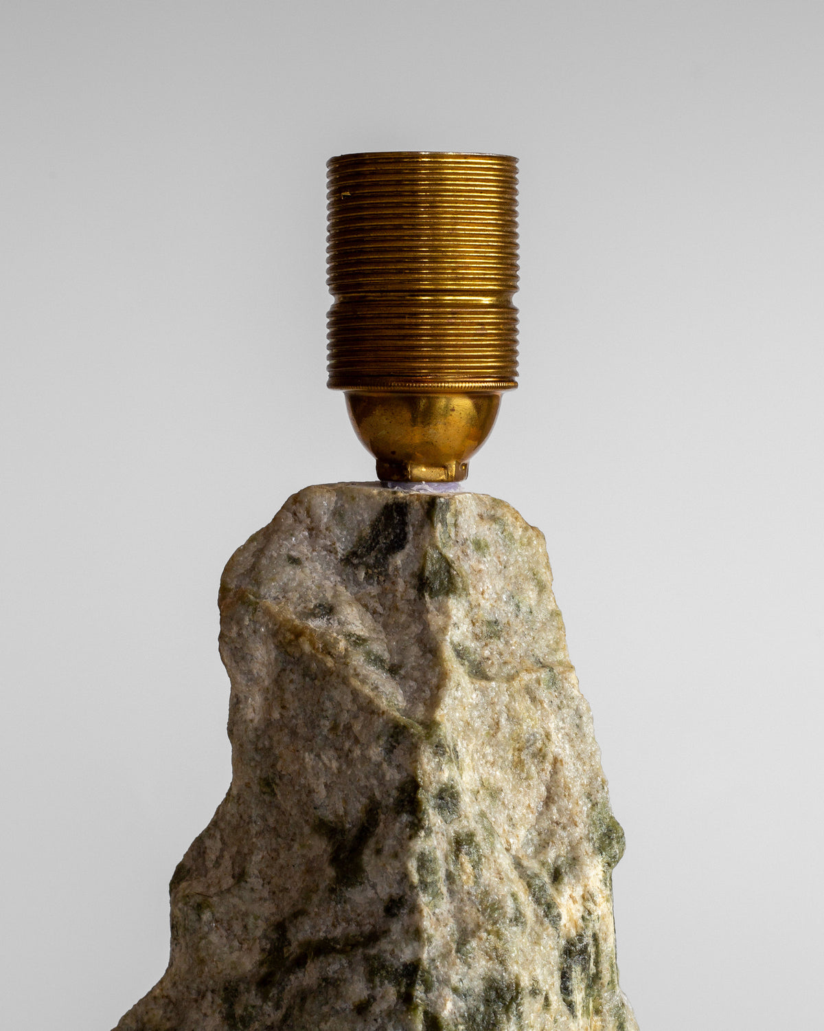 A stack of golden, cylindrical rings balanced atop a rugged, gray rock captures the sleek elegance of the Spigel Marble Stone Table Lamp against a plain white background.