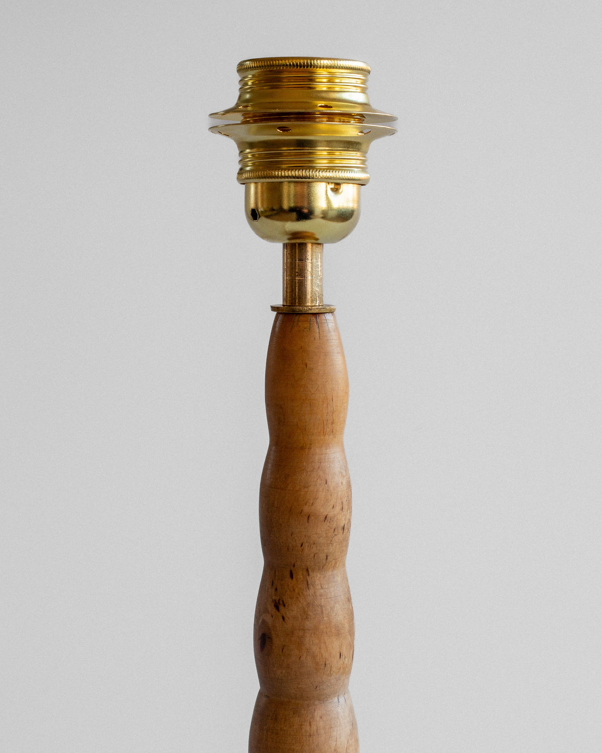 The Spigel Turned Birch Table Lamp from Sweden features a wooden base with a natural finish, knobby design, and brass fixture. The ridged socket caps off this simple yet elegant lamp stand.