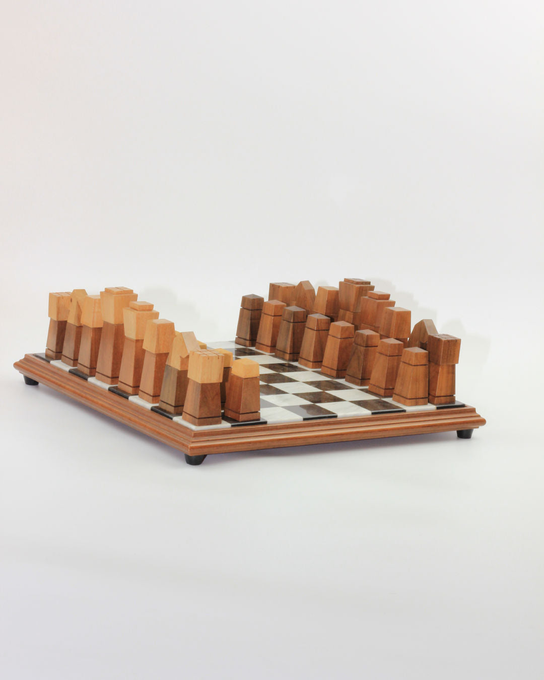 The Boga Avante Shop's Wooden and Marble Chessboard showcases vintage, hand-carved wooden pieces with geometric, blocky designs arranged on a checkered board. Crafted from various shades of wood, the pieces and the marble board create a striking contrast against the white background. The set stands gracefully on four sleek legs.