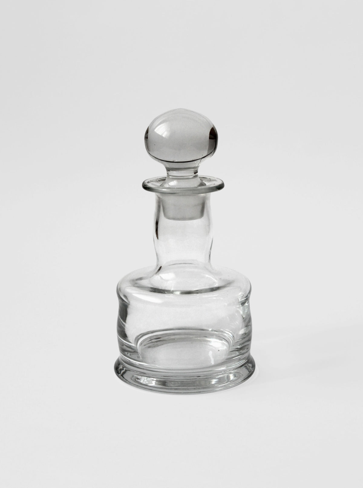 Clear glass mini decanter with rounded stopper, elegant profile view