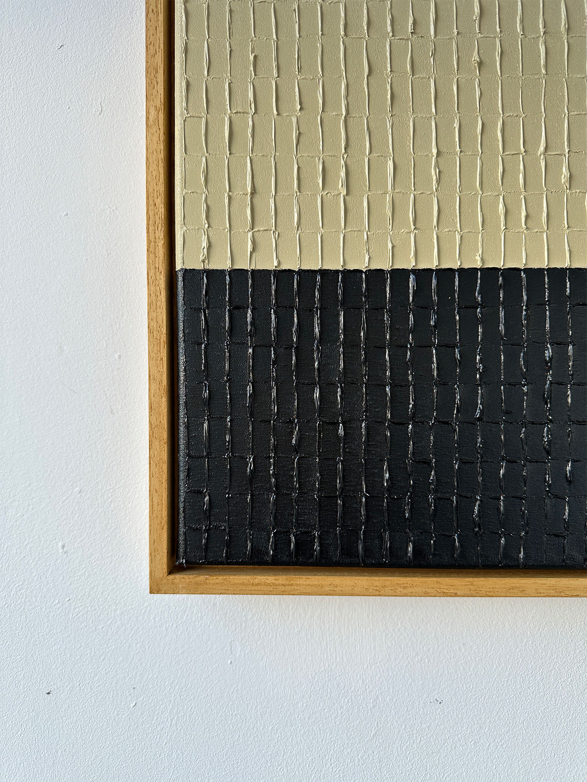 Buff Black by Roi Elmaliah is an oil on canvas featuring two halves: beige on top and black below, divided by black grid lines. Framed with a wooden border, it adds a touch of Amsterdam's elegance against a white wall.
