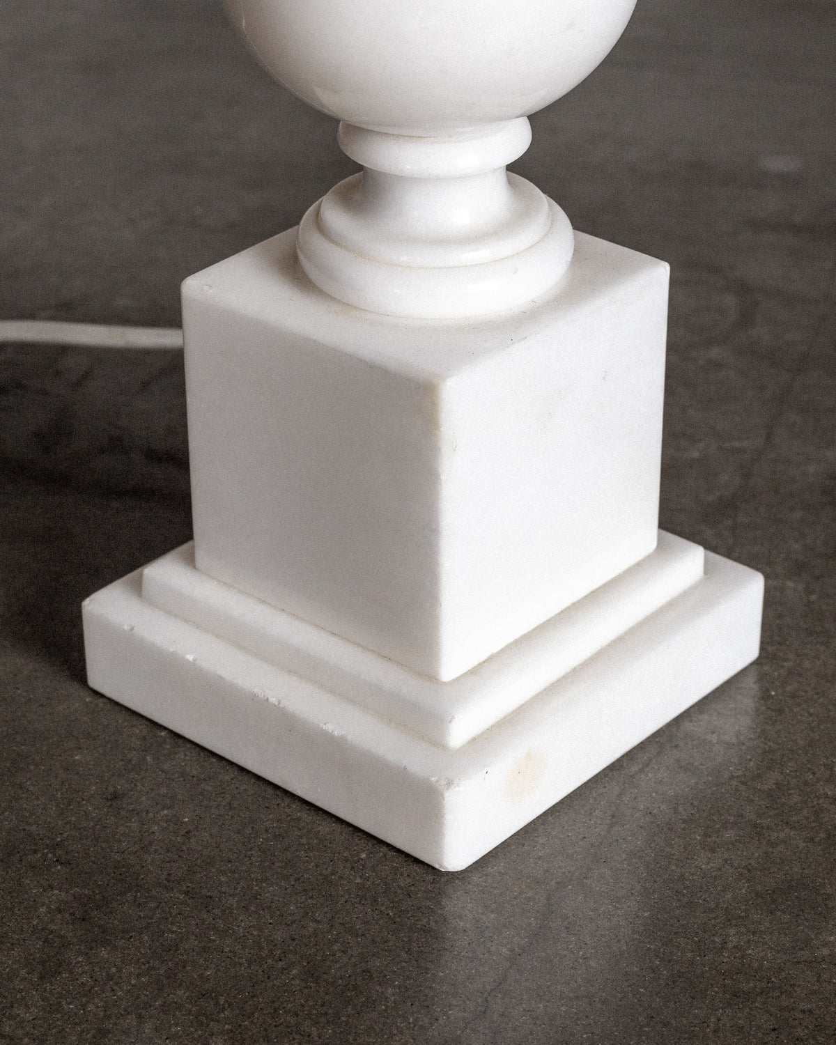 A close-up of the Spigel Italian Alabaster Chess Knight Table Lamp, 1970s, featuring a hand-carved design and white marble square tiered base, rests on a gray concrete floor with an electric cord partially visible behind.