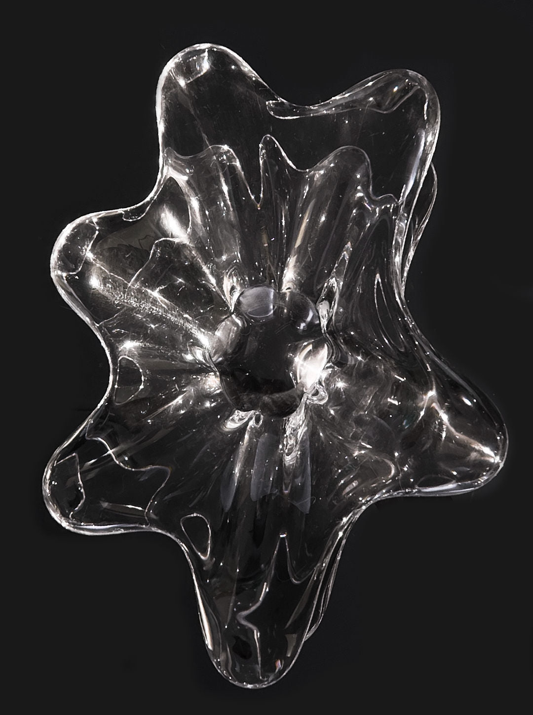 The Les Objoies Crystal Baccarat Cup features an abstract glass design with wavy edges and a hollow center in a star or flower shape. Set against a black backdrop, it reflects light brilliantly, resembling a modern vessel and epitomizing crystal artistry.