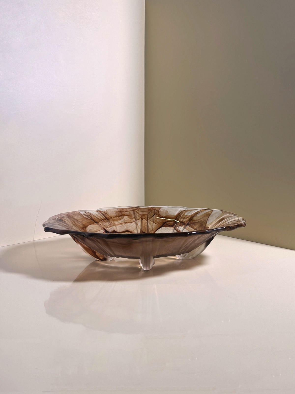 The German Art Deco Cloud Glass Bowl circa 1930 by Dodo Vintage, featuring wavy edges and brown-beige swirls, rests on a glossy white surface near the junction of two pale walls.