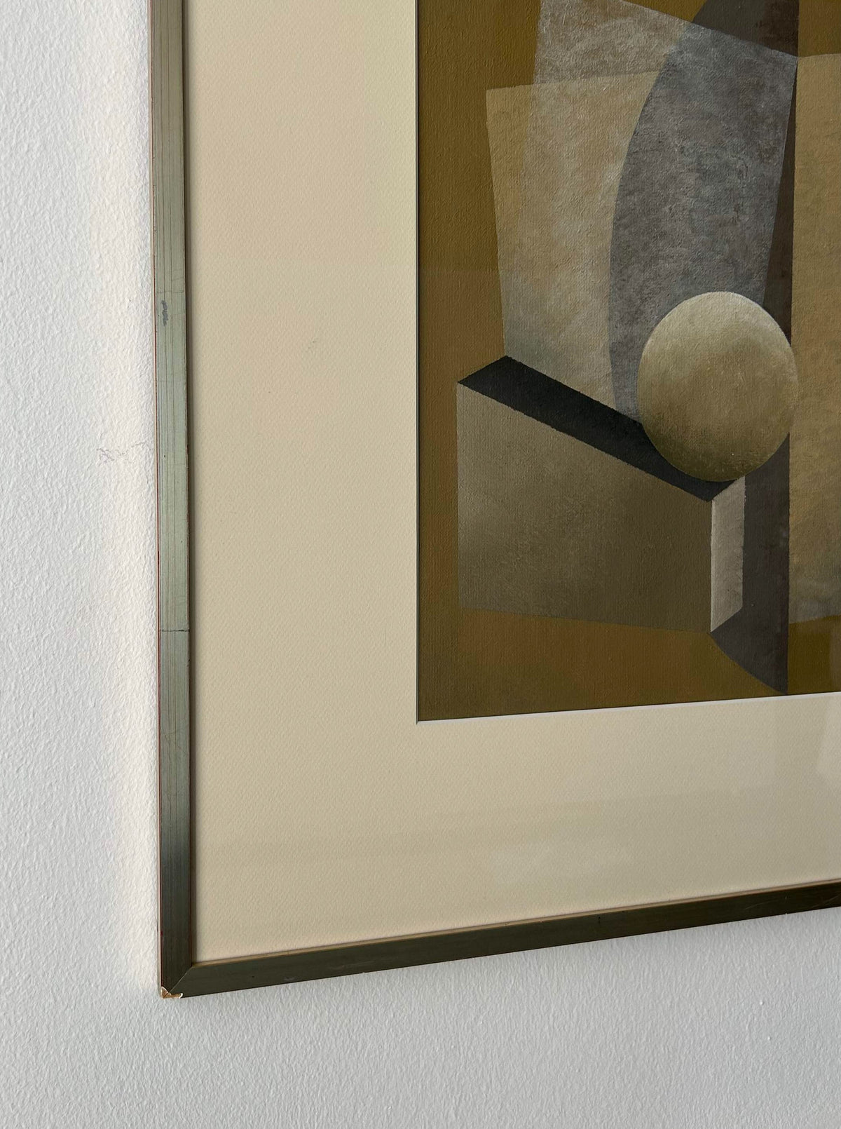 A close-up of a framed geometric abstract acrylic painting on a white wall. The artwork features shapes such as rectangles, triangles, and a sphere in muted tones of brown, beige, and gray. The frame's metallic edge hints at a vintage design. Dimensions: 50x60cm. Product Name: "New Gold Dream" Painting, 2023 Brand Name: Iris Bavelaar