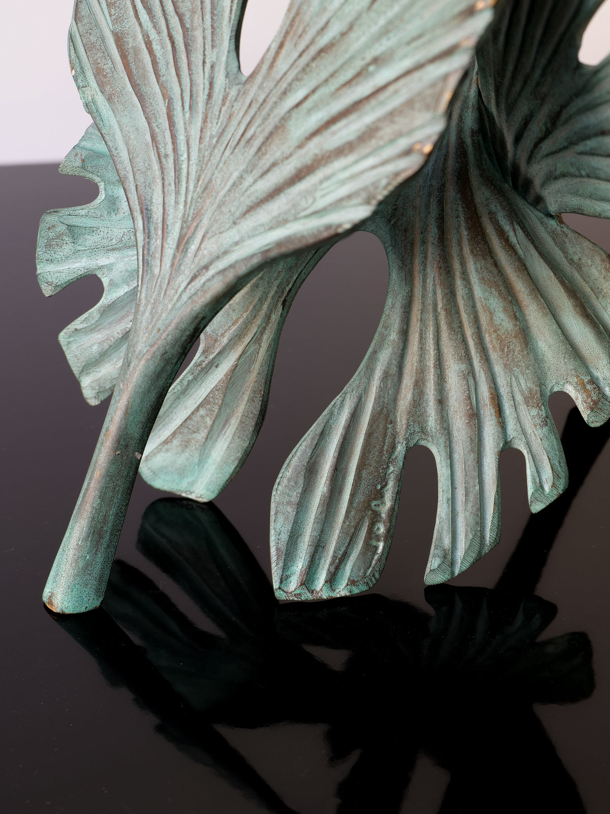 A close-up of the Bronze Ginko Biloba Sculpture by Collection apart, featuring large ginkgo leaf-like forms with a textured, weathered surface casting a shadow on its glossy black base.