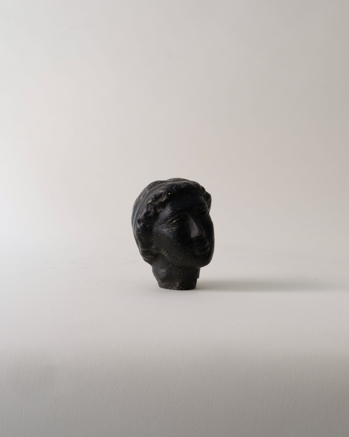 The Venus Stone Sculpture by Collection apart is a compact, dark stone composite bust of a classical head with short, wavy hair, set against a light background. Its ancient, weathered look captures the timeless elegance of Venus.