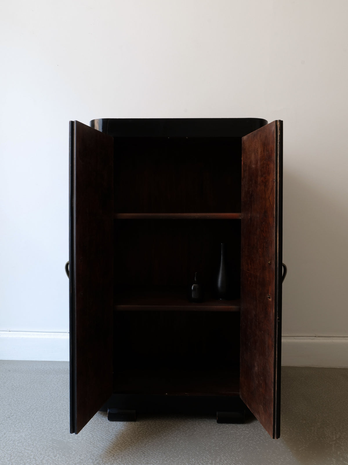 Against a plain white wall on a light gray floor, the French Deco Cabinet 1930s by Collection apart stands open, revealing two shelves. A single black lacquer vase is displayed on the bottom shelf, highlighting its Art Deco elegance.