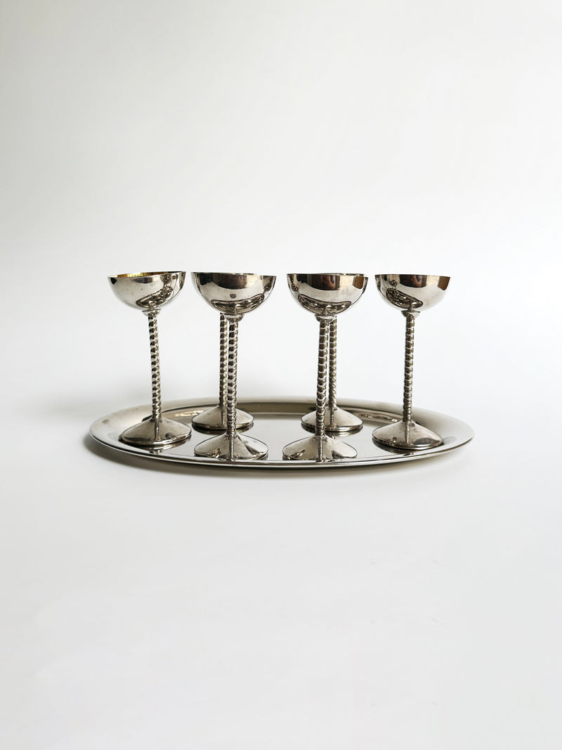The Art Nouveau liqueur goblet set by Dodo Vintage features a quartet of silver goblets with intricate stems, evoking the elegance of the Art Nouveau era. They are beautifully arranged on an oval silver tray. Against a plain white backdrop, the gleaming reflective surfaces of both the goblets and tray are showcased, creating an aesthetic that is both minimalist and refined.