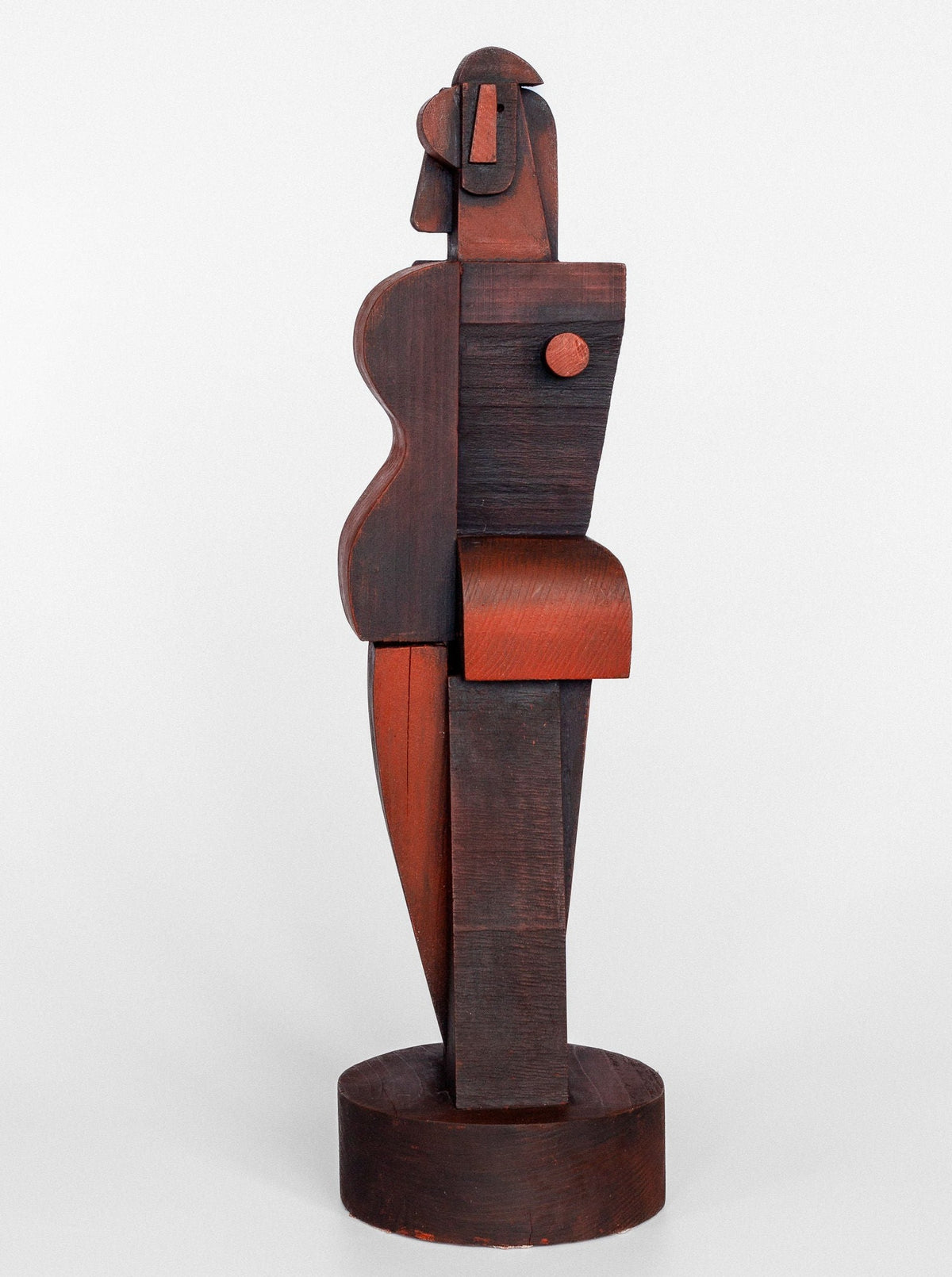 The Cubist Sculpture by Spigel showcases a stylized human figure standing on a circular base. Inspired by cubism, this wooden abstract piece features geometric shapes such as a rectangular torso, cylindrical head, and curved elements, presented in a palette of dark brown and reddish hues.