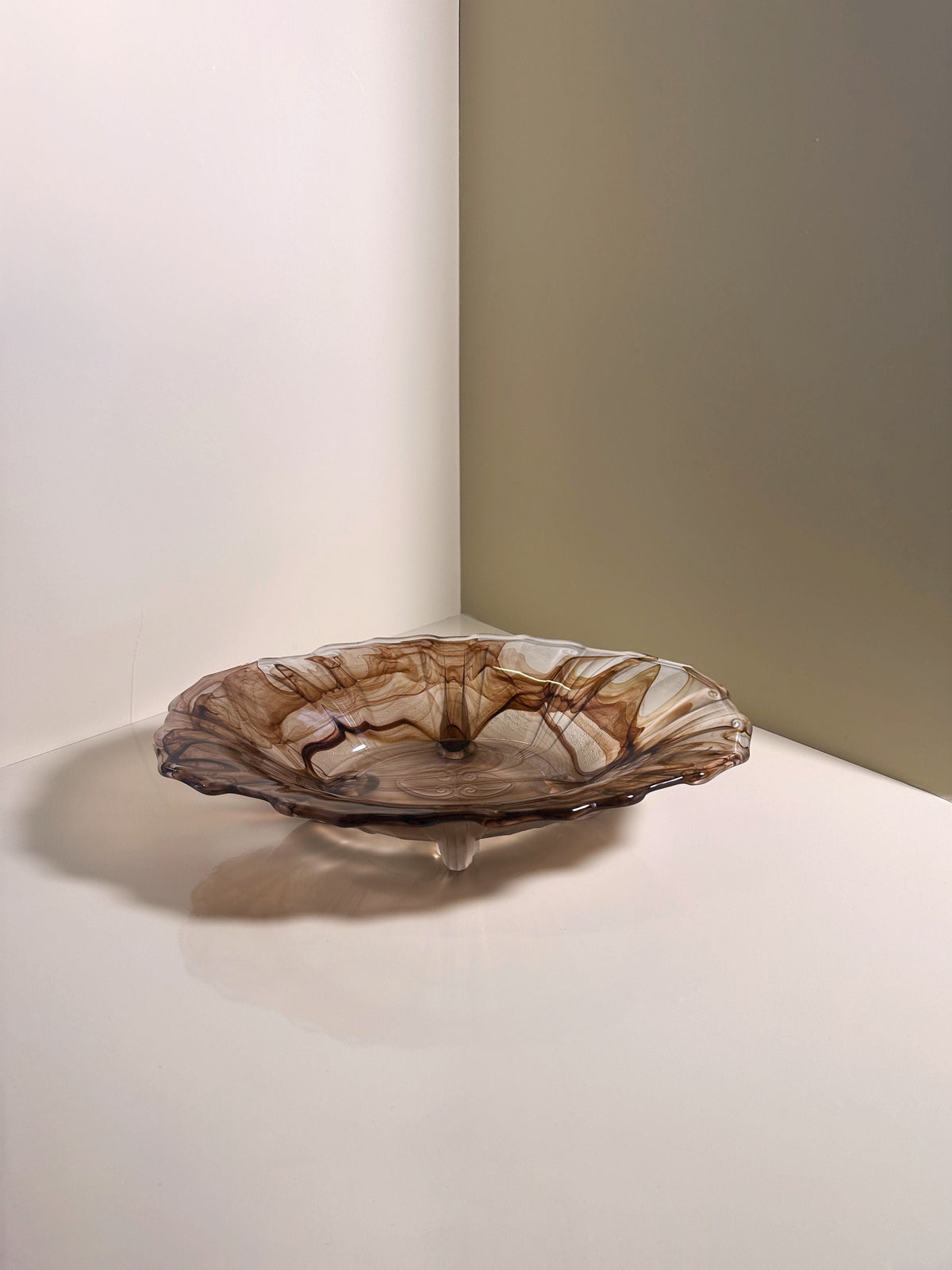 A German Art Deco Cloud Glass Bowl circa 1930 by Dodo Vintage, featuring wavy translucent edges and swirling brown patterns, sits on a glossy white surface against light tan and white walls.
