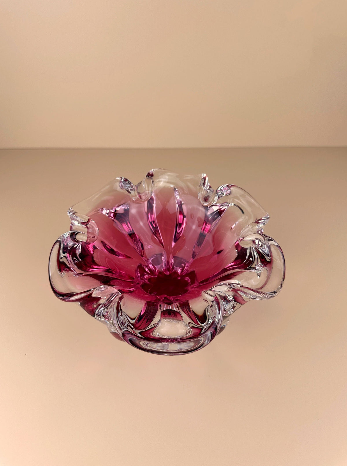 A pink Bohemian Cranberry Red bowl by Josef Hospodka with delicate, translucent petals, crafted by Bohemian glassmakers and displayed against a soft, off-white background. The bowl's design mimics a blooming flower with