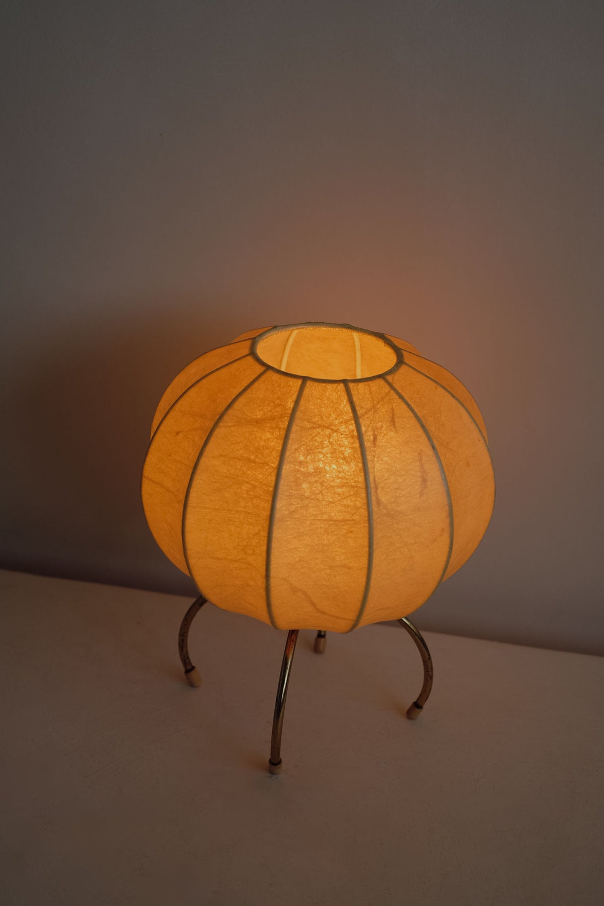 Cocoon table lamp with orange paper shade on metal legs, illuminated
