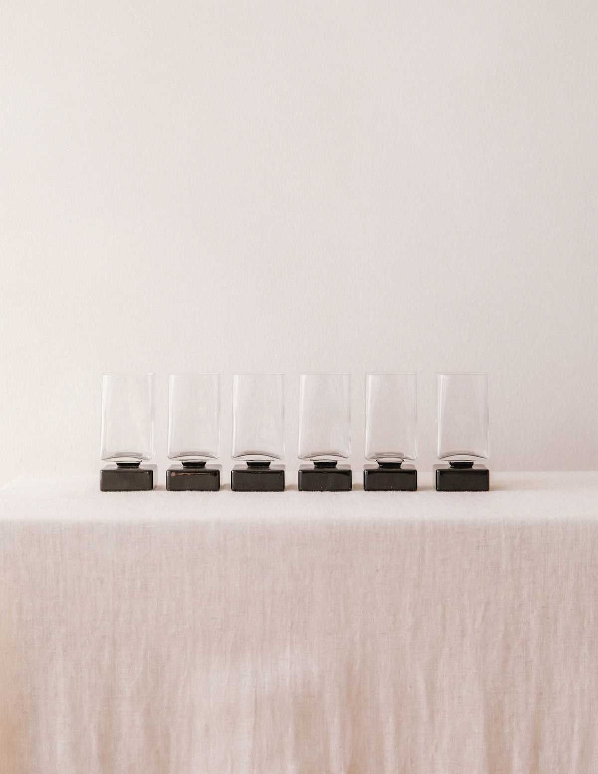 Six clear glass liqueur glasses with black bases in row