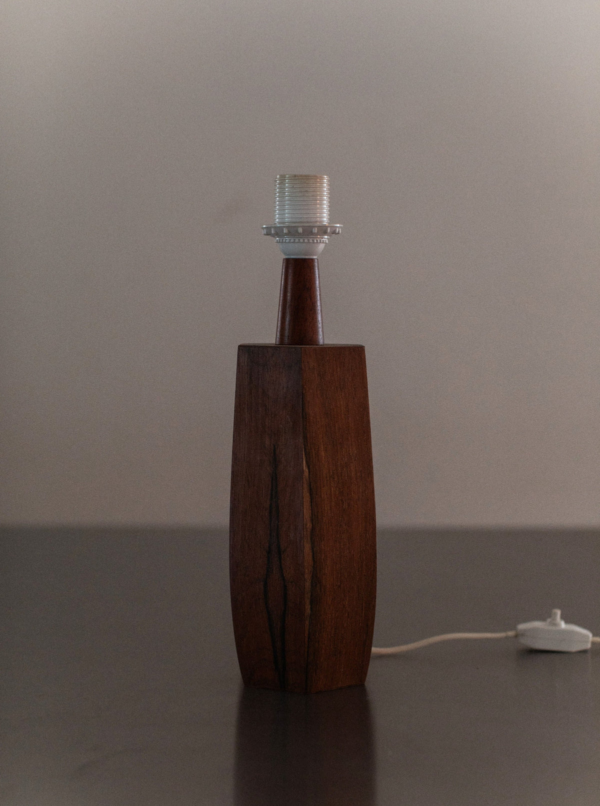 A 1940's Wooden lamp by Out For Lunch with a minimalist, mid-century design, featuring a rectangular shape and natural wood finish. The top has a light bulb socket without a bulb. Attached is a white cord with a switch. The background is plain and softly lit, highlighting its impeccable craftsmanship.