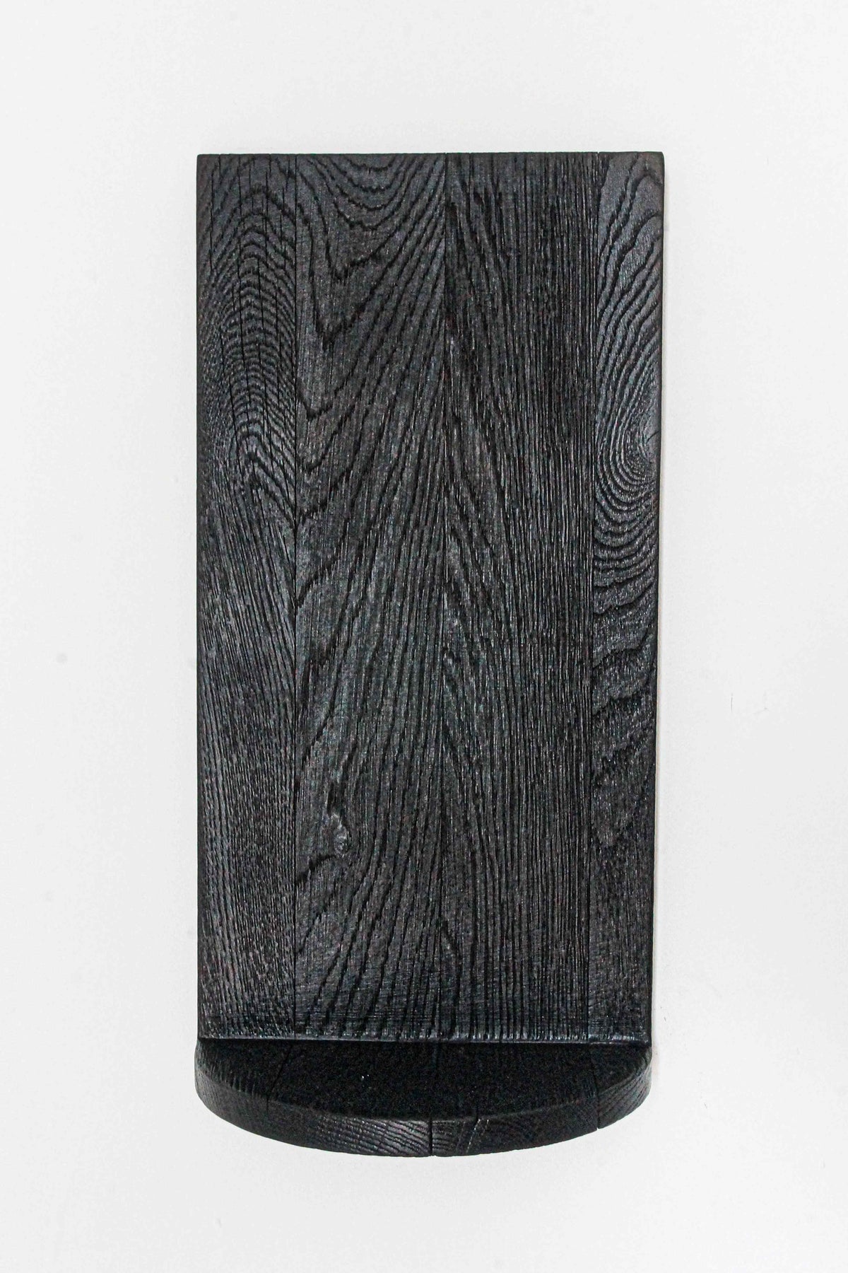 The Megaron - Minimalist Shelf in Wood (Small) by COSEINCORSO features a black solid oak design with a curved bottom edge and visible wood grain, mounted against a white background for a sculptural, handcrafted look.