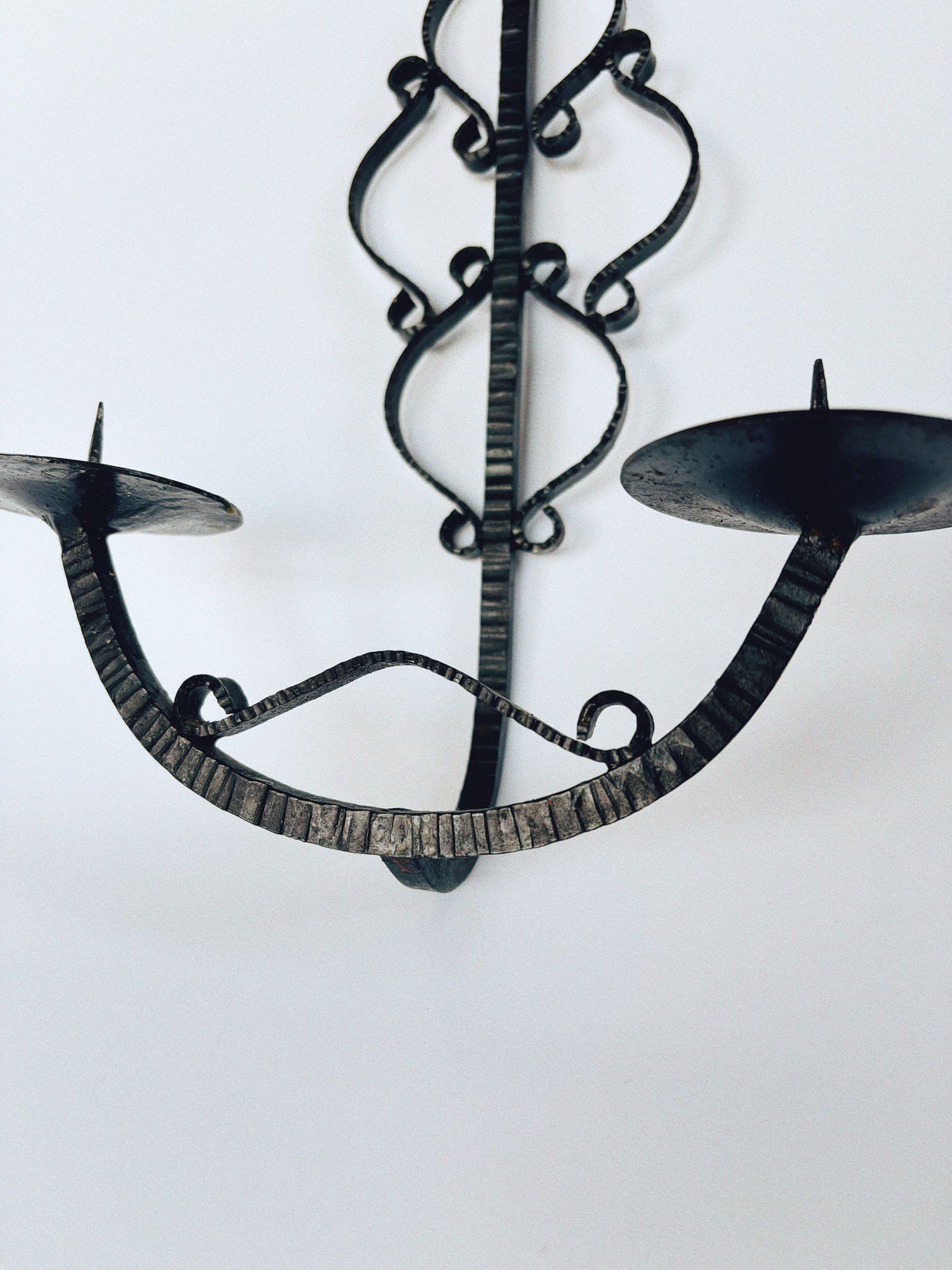 A close-up of the Huerto Metalwork Wall Candleholder from Poland, featuring vintage hand-forged metalwork, decorative curved designs, and two candle holders against a white background.