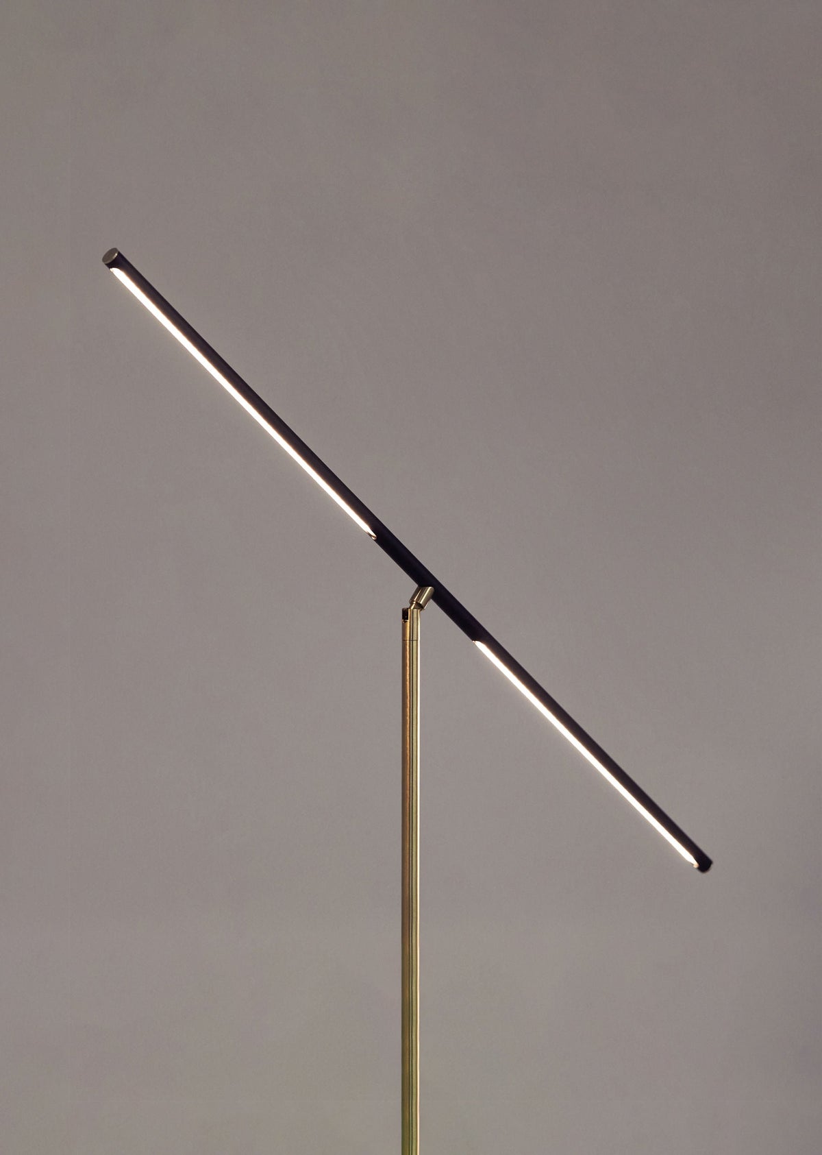 The 'T- Lamp' Floor Lamp by Heako Studio features a minimalist design with a thin, angled LED bar on a slender vertical stand, creating sculptural light and modern style against any plain background.