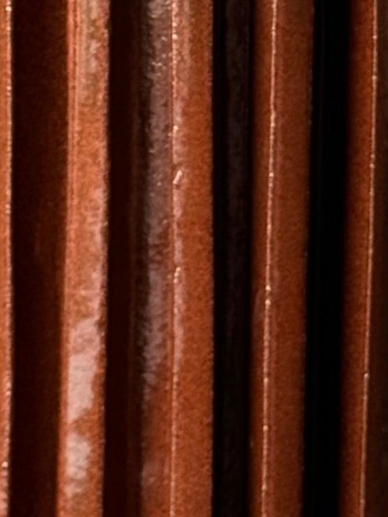 Close-up of several vertical brown ceramic tiles with a glossy finish from Devin Wilde’s Vessel No. V, reflecting light and creating subtle highlights and shadows between the grooves.