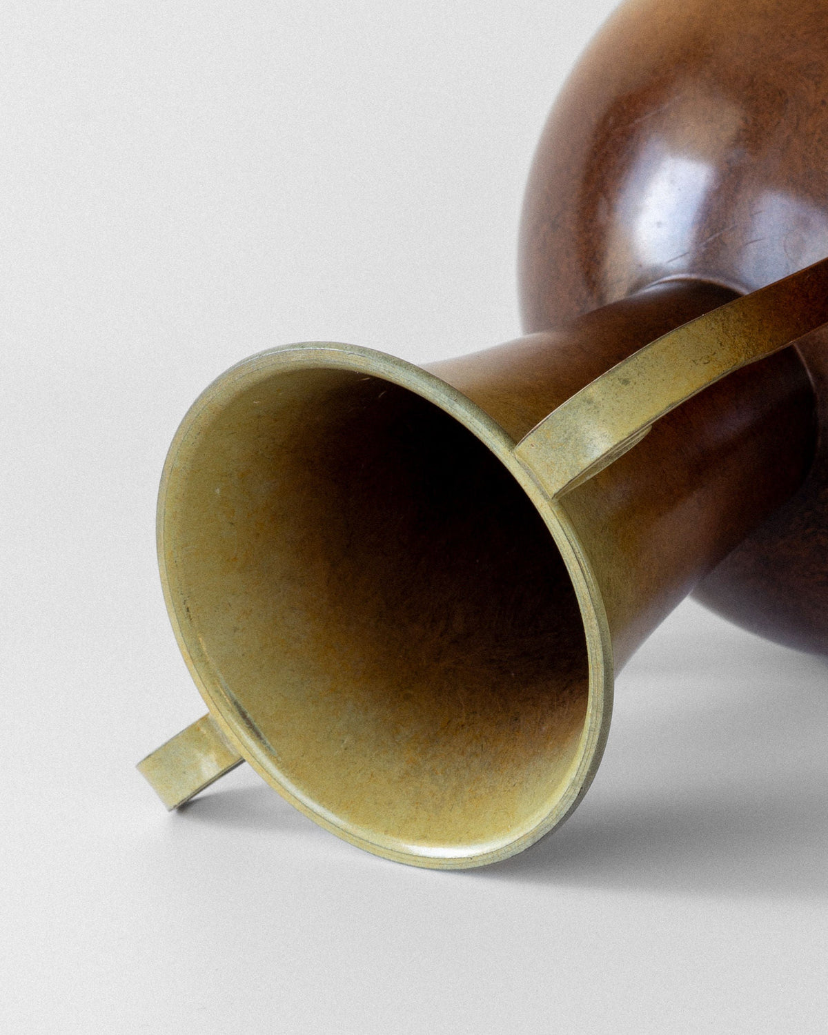 A close-up of the Spigel Swedish Art Deco Bronze Vase lying on its side, highlighting its flared bell and smooth, reflective bronze surface against a plain, light background.