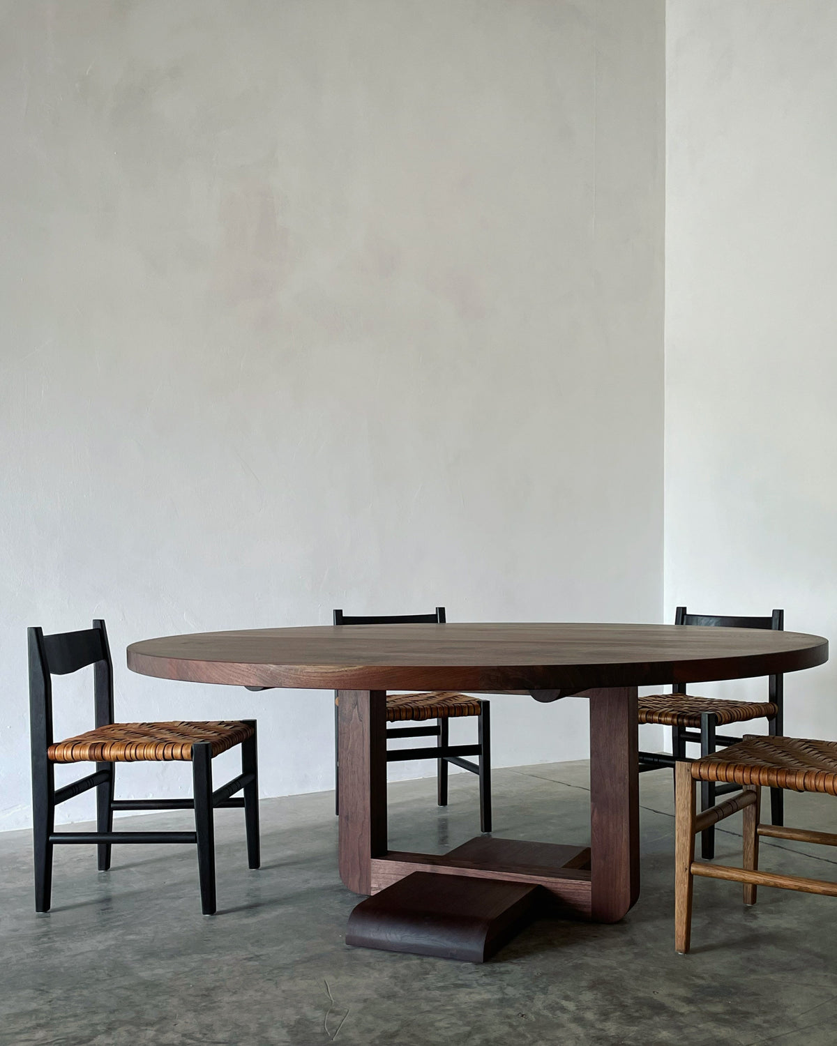 Alpen Round Dining Table — side angle with dark wood and woven chairs