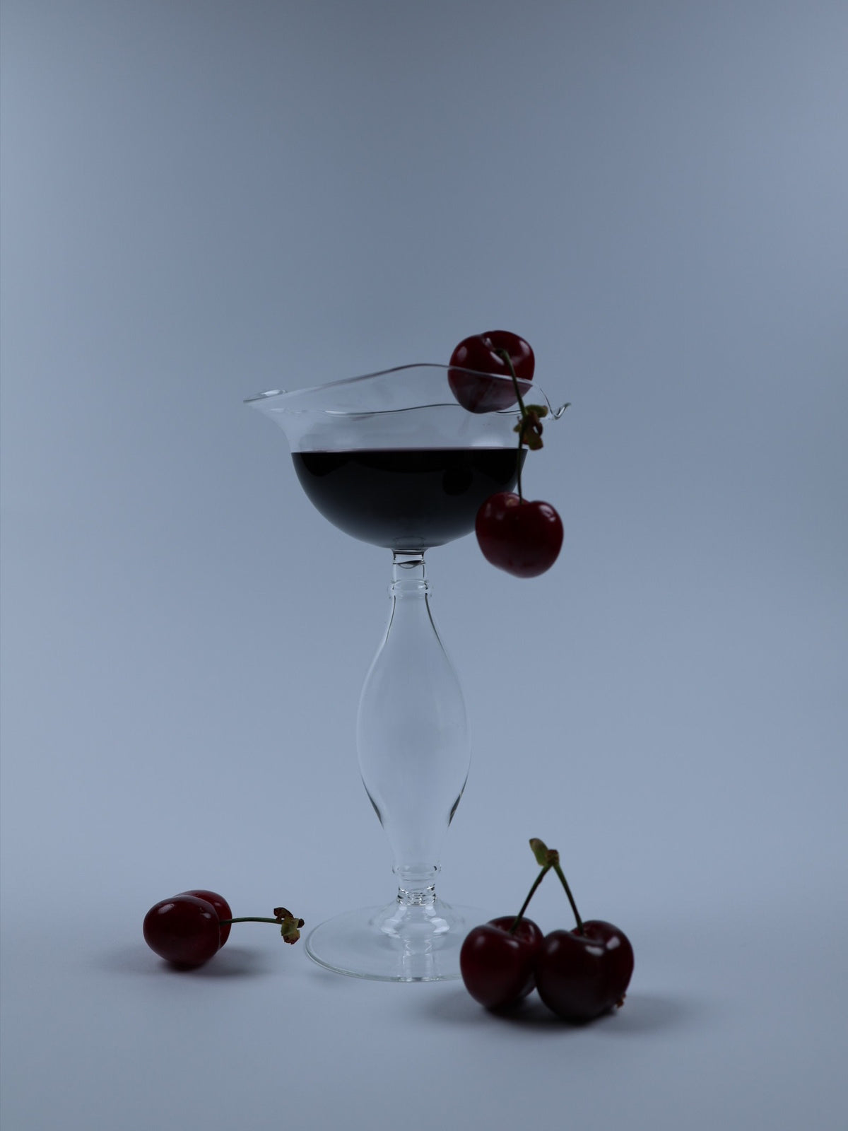 Crater wine glass with dark liquid and cherry garnish detail