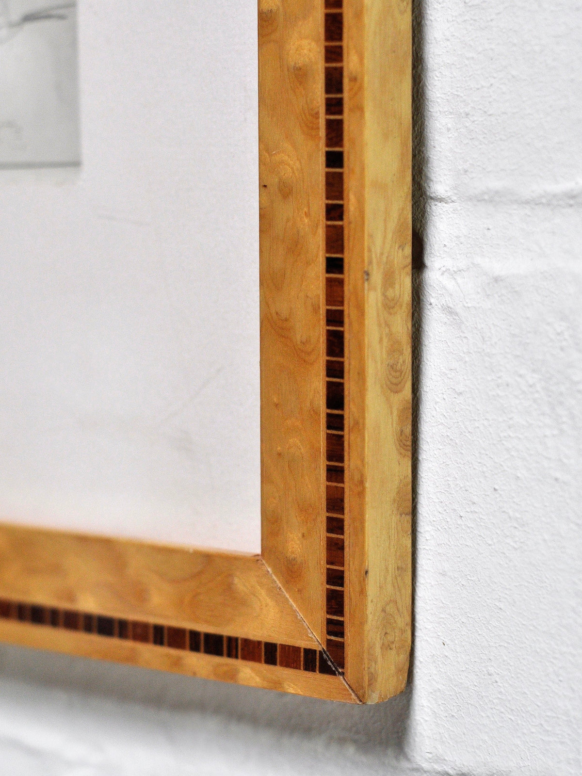 Close-up of an Introverso wooden frame with decorative inlay, displaying a corner of the "André Lhote (1885–1962) Drawing in Pencil," hanging on a white textured wall.