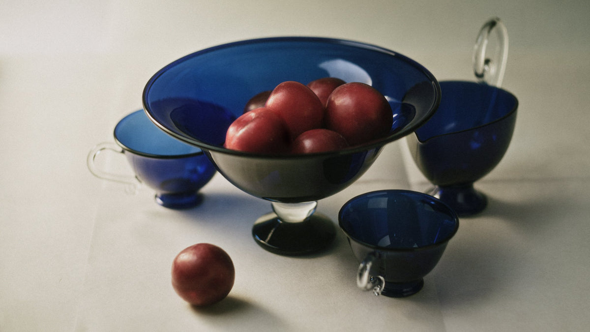 Fruit Bowl — modern glass bowl with red plums on white surface