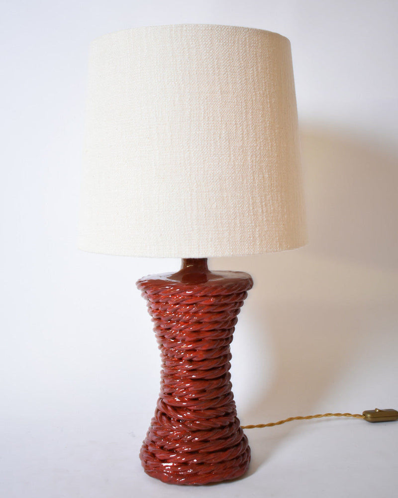 The "Kasaï" Red Ceramic Table Lamp by Barracuda Interiors features a glossy, textured dark red base resembling twisted rope and a wide off-white fabric shade. This plug-in lamp with a twisted cord is shown against a plain white background.