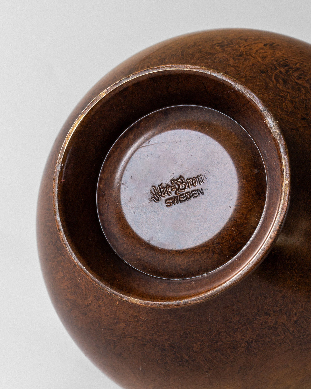 Close-up view of the bottom of a Swedish Art Deco Bronze Vase by Spigel, featuring engraved text at the center base. The plain background emphasizes Spigel's elegant craftsmanship.