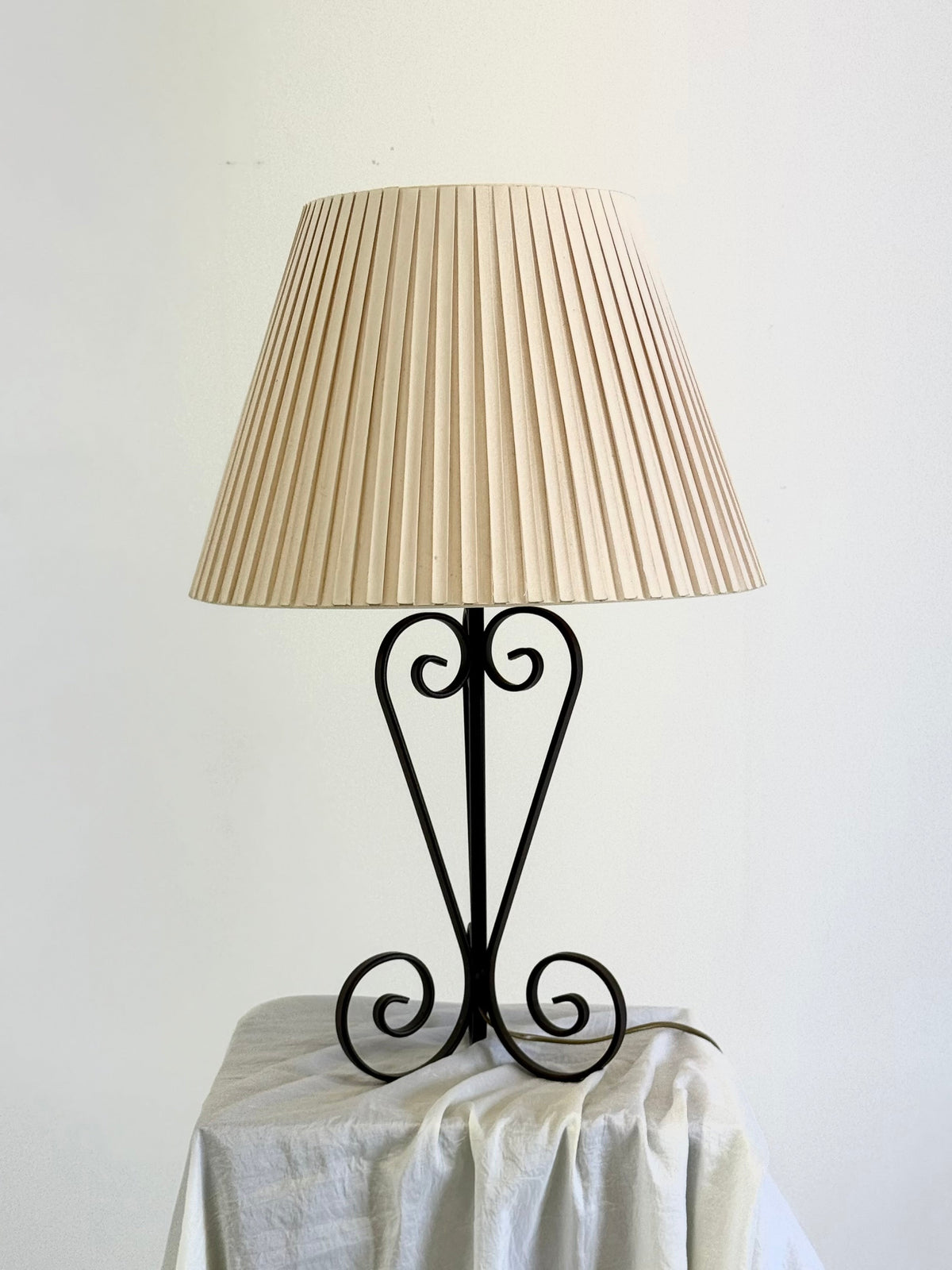 Vintage wrought iron table lamp in a swirl shape with a pleated shade — close-up