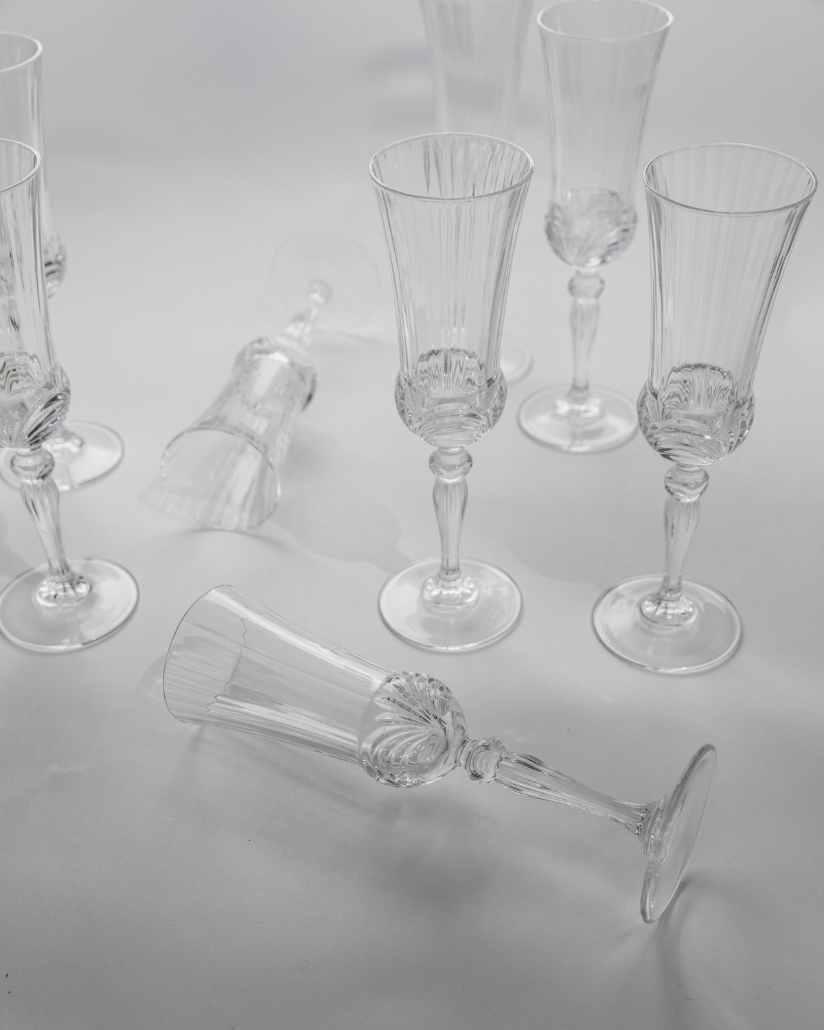 Crystal champagne flutes arranged on white surface, one glass fallen