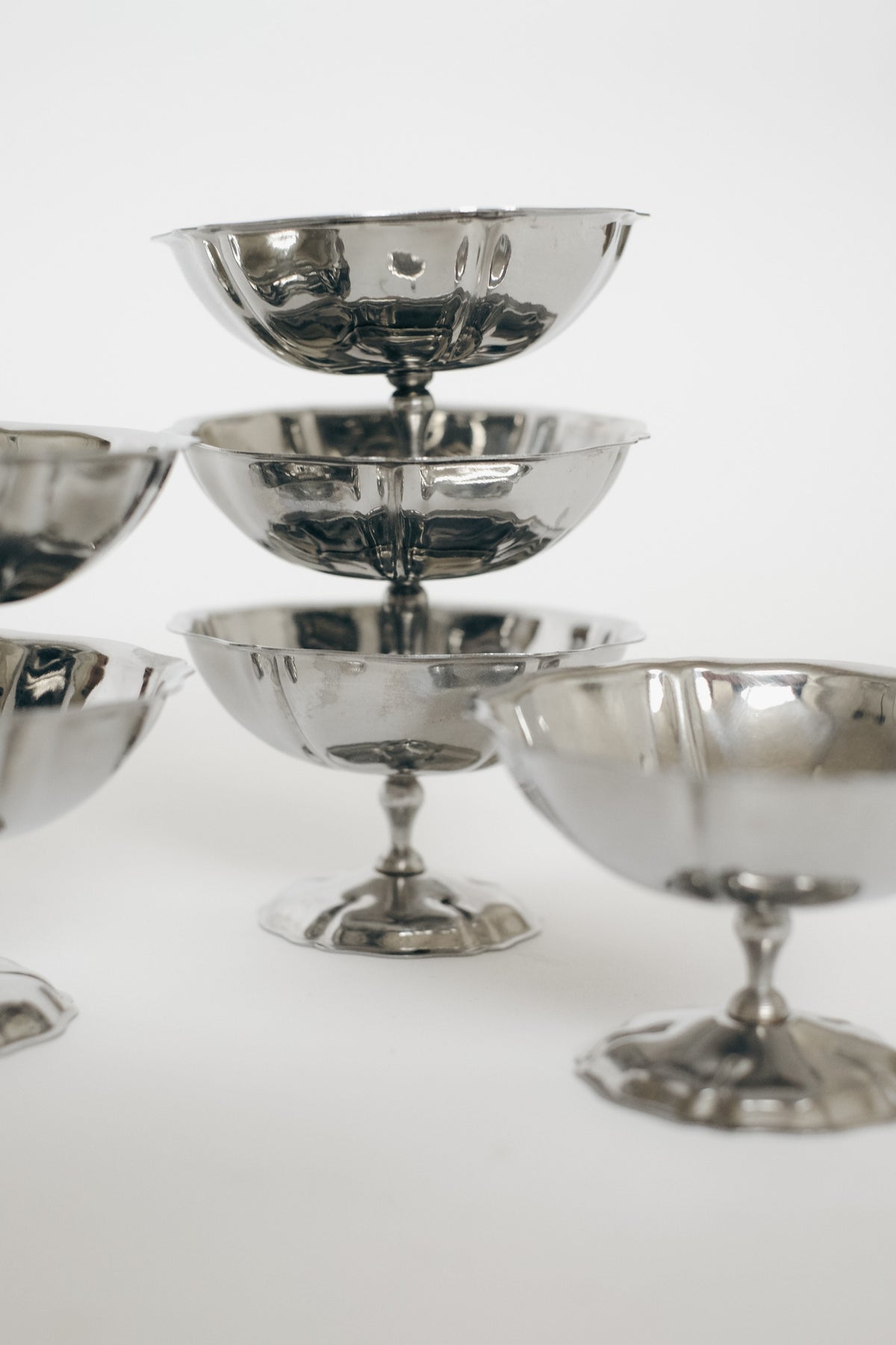 A set of six shiny, silver vintage stainless steel ice coupes by septembre studios is arranged in a staggered, layered formation against a plain white background.