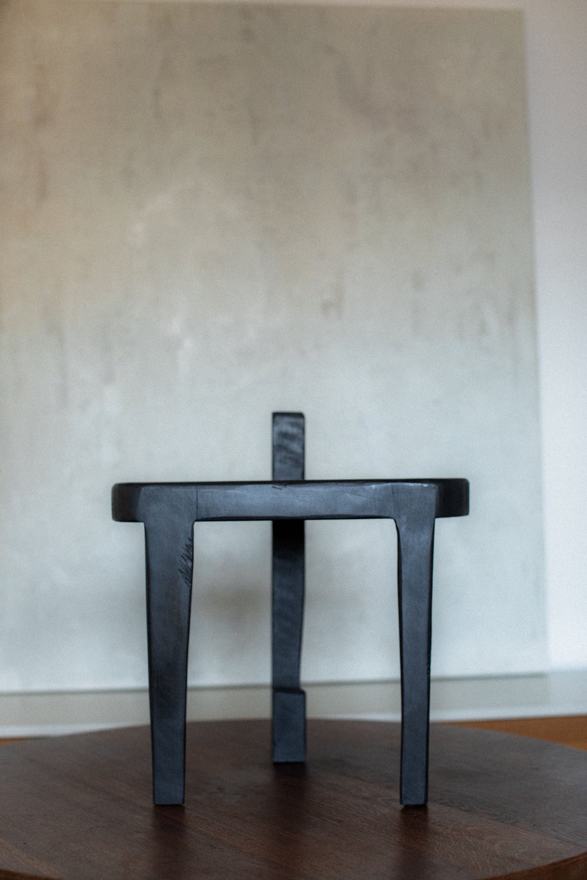 Black wooden stool with round seat and three legs, minimalist design