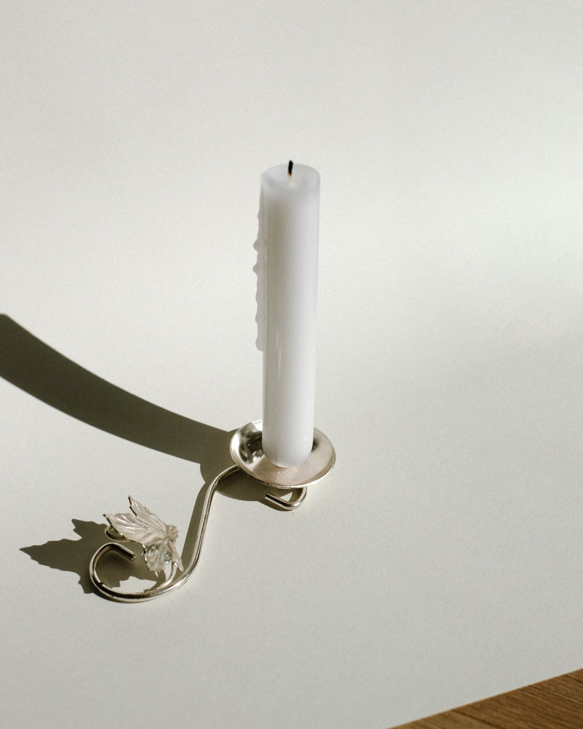 Silver-plated candle holder with decorative leaf detail casting shadow