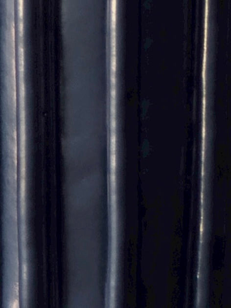 Close-up of dark, shiny vertical lines with reflective highlights evoke the sleek textures of Vessel No. II by Devin Wilde.
