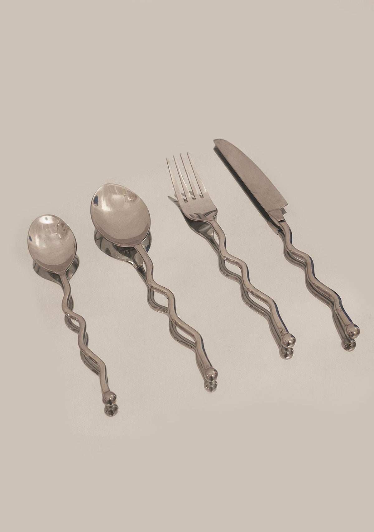The Les Objoies Set of 4 Zig-zag Cutlery includes a spoon, soup spoon, fork, and knife with wavy twisted handles, arranged side by side on a plain light surface.