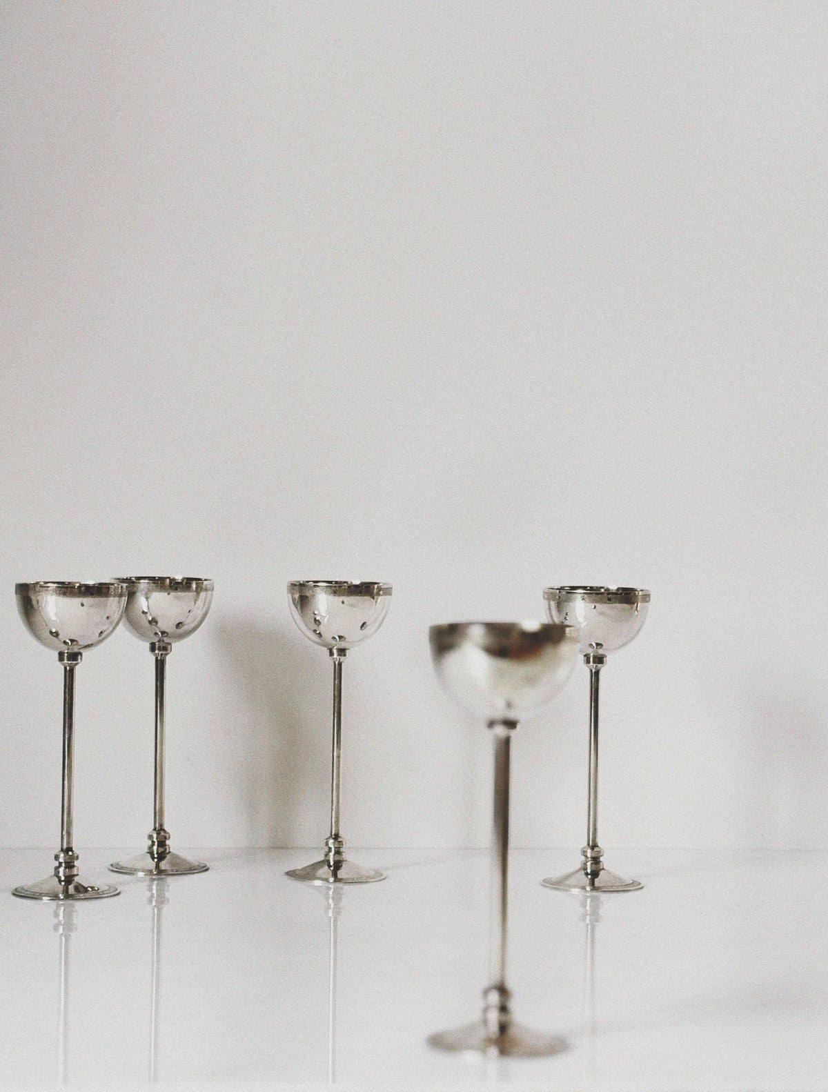 Silver plated coupe glasses with decorative stems on reflective surface