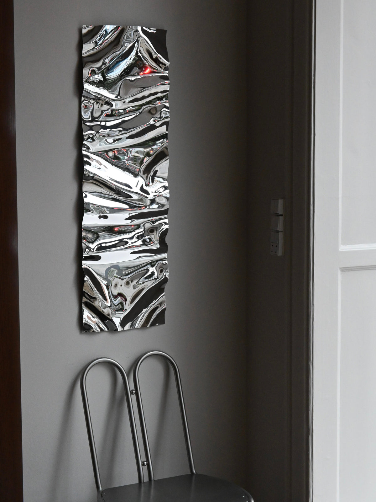 Psychedelic Mirror Long — mounted on wall beside minimalist chair