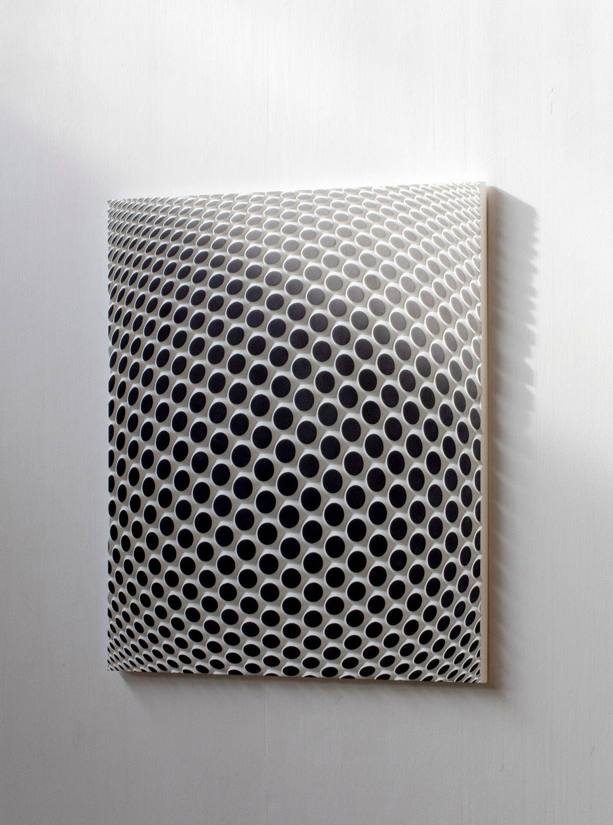 Ommatidium by Studio Arno Hoogland is a square artwork with a grid of raised, ommatidium-like circular holes that form an optical illusion of a 3D bulging sphere on a white background, with shadows adding depth to the effect.