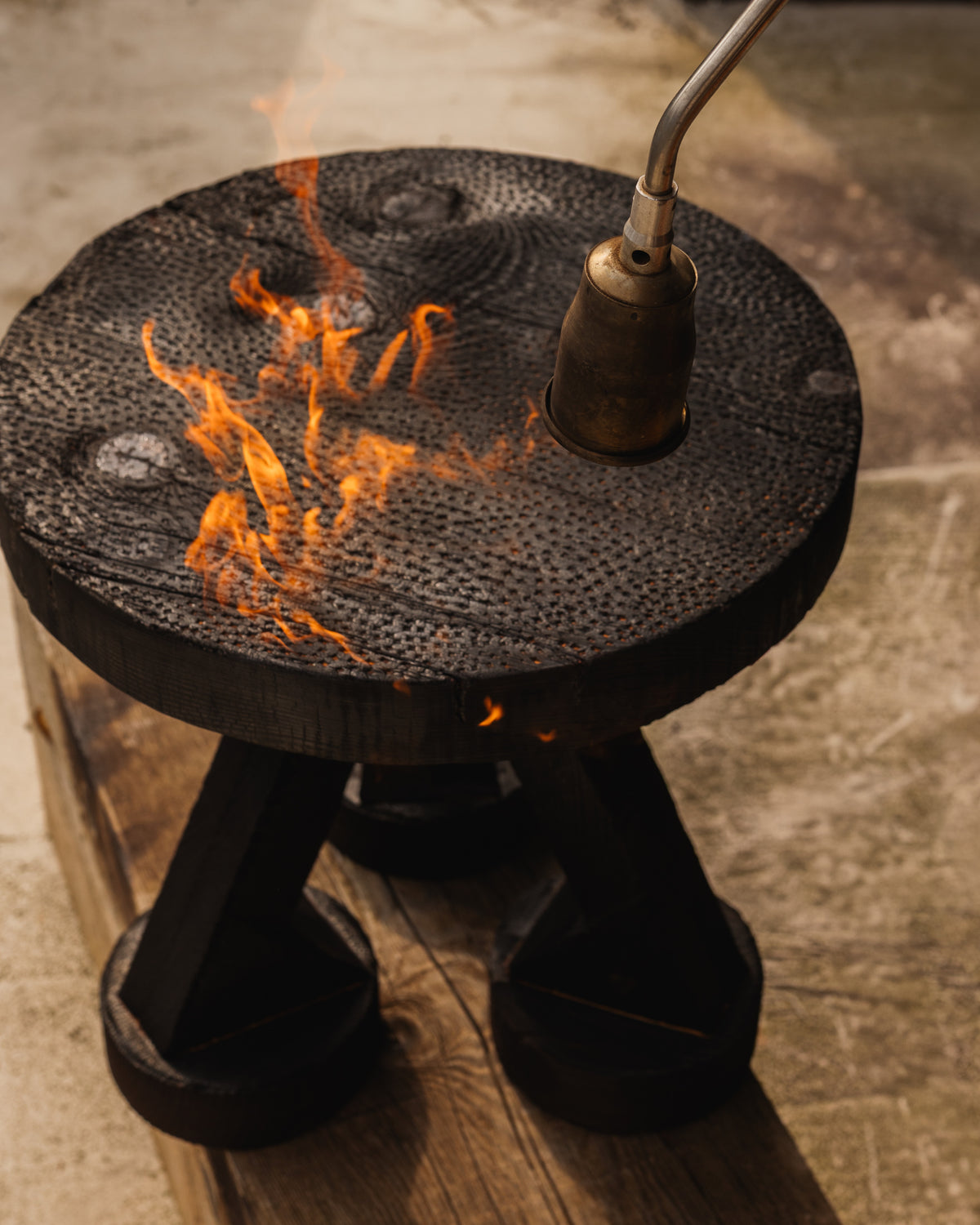 ABORA burnt wood end table with forge torch creating flames on surface