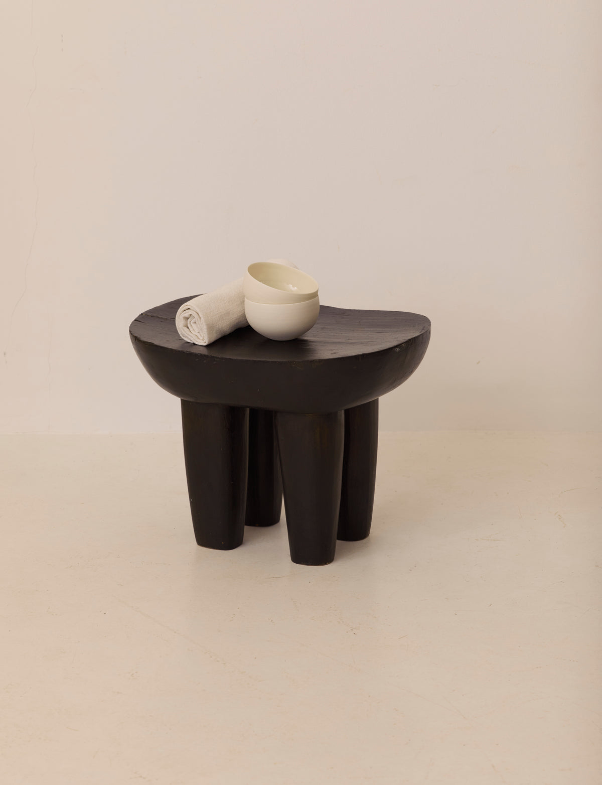 Vintage Senufo Monoxyl African Stool in Black / Wenge — angled view with white towel and bowl