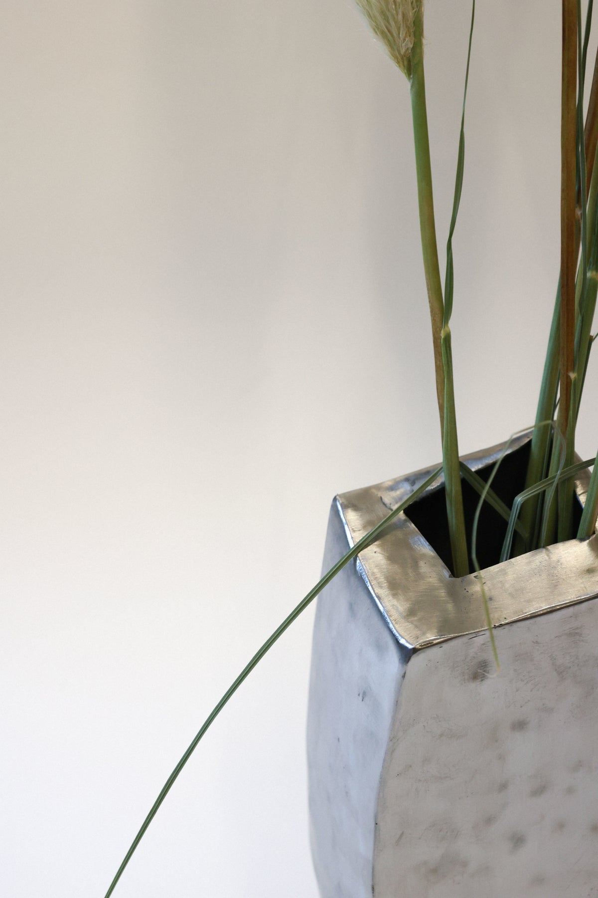 Hammered steel vase detail showing textured metallic surface and grass stems