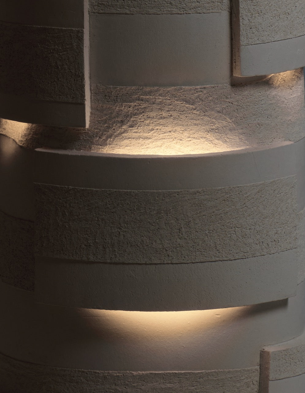“Bricks” Table Lamps in Ceramic by Katia Langeard softly illuminate surfaces, their warm glow highlighting textured layers and horizontal grooves, creating a dynamic play of light and shadow across the space.