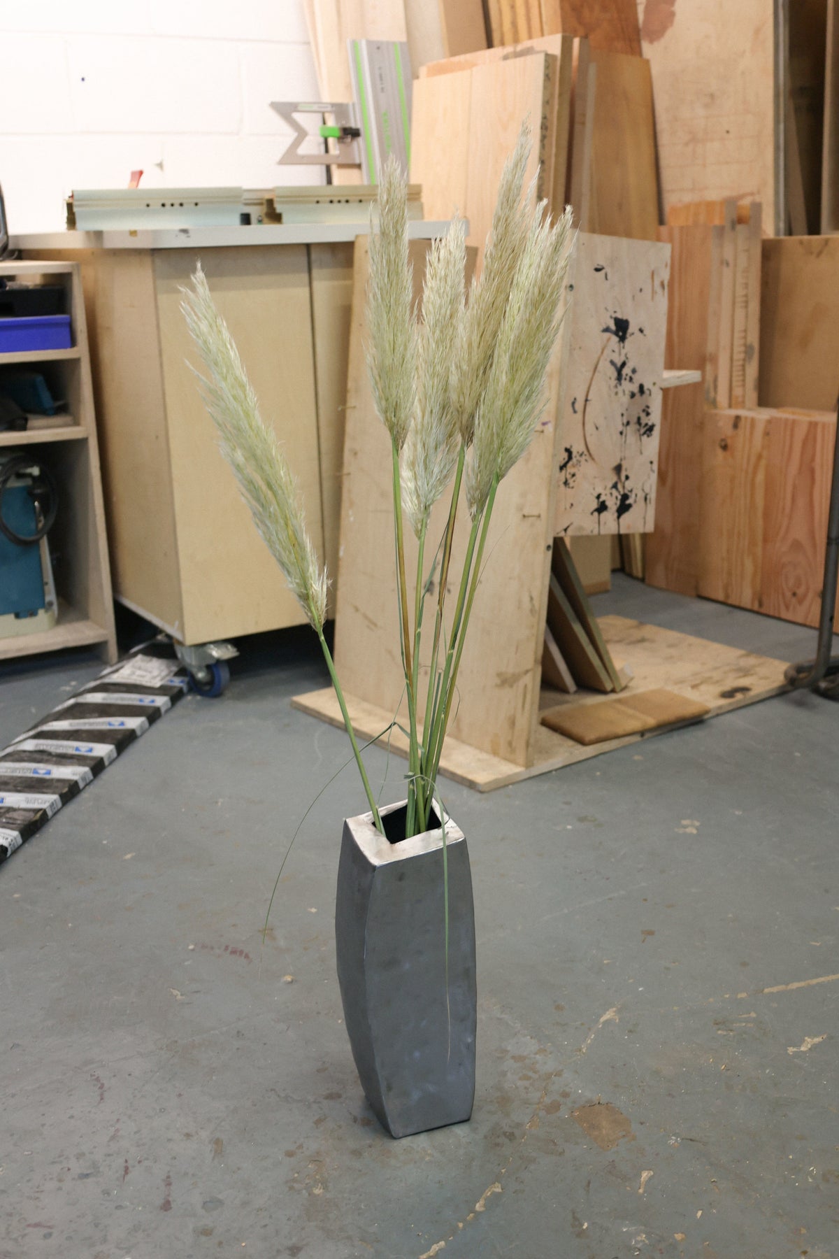 Tall grasses in dark hammered steel vase in woodworking studio