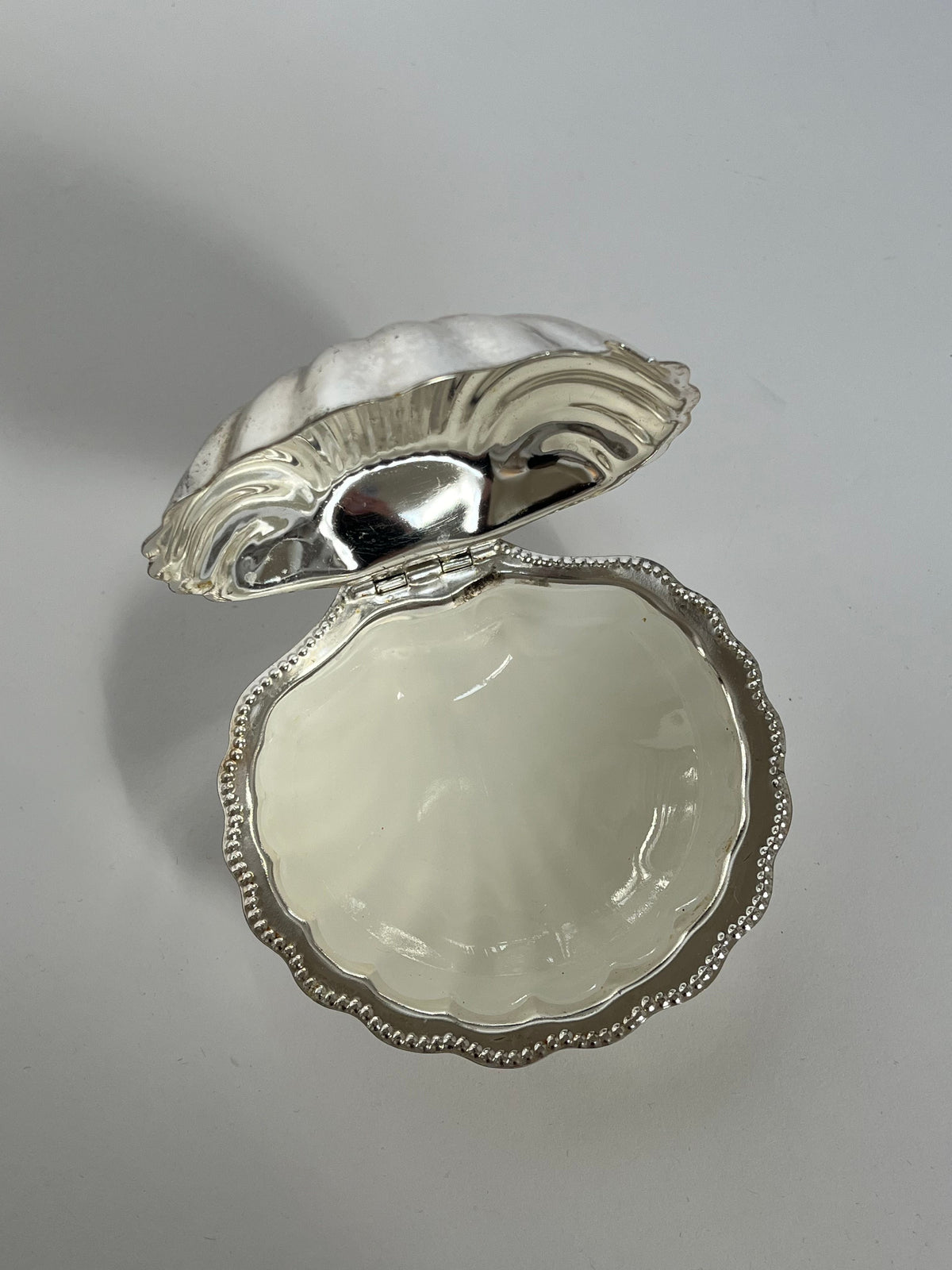 The septembre studios Shell Shaped Butter Dish features a shiny silver outer edge and a smooth pearly white interior, elegantly displayed open on a simple white surface.