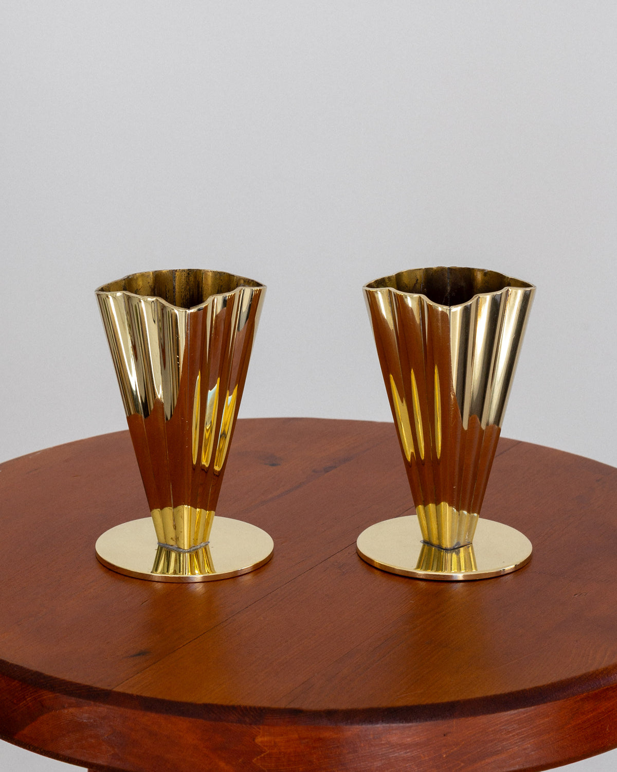 Pair of fluted brass vases on round wooden table, profile view